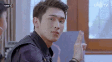 a young man is sitting in front of a window and making a peace sign with his hands .