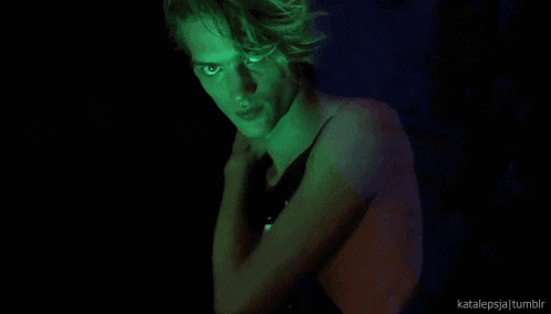 a man without a shirt is standing in a dark room with a green light shining on him .