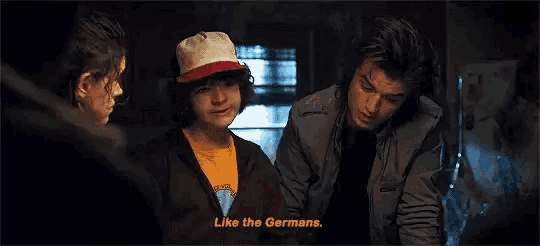 a group of people are sitting around a table talking to each other and one of them is wearing a hat .