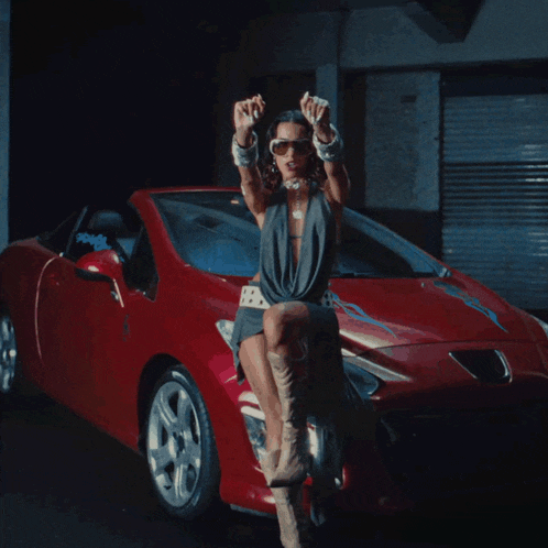 a woman is sitting on the front of a red sports car