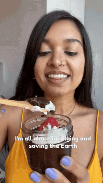 a woman in a yellow tank top is holding a jar of chocolate pudding with strawberries and whipped cream ..