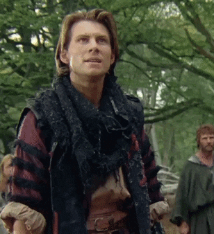 a man with a scarf around his neck stands in the woods