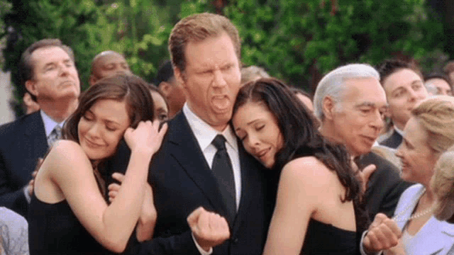 a man in a suit and tie is hugging two women