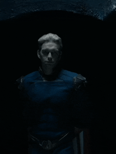 a man in a blue superhero costume stands in the dark