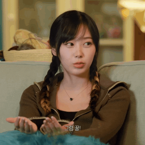 a woman with braids is sitting on a couch with a foreign language written on the bottom of her face