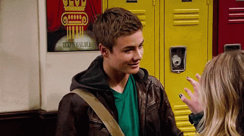a boy in a leather jacket is talking to a girl in front of a yellow locker .