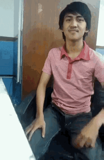 a young man wearing a pink shirt is sitting in a chair