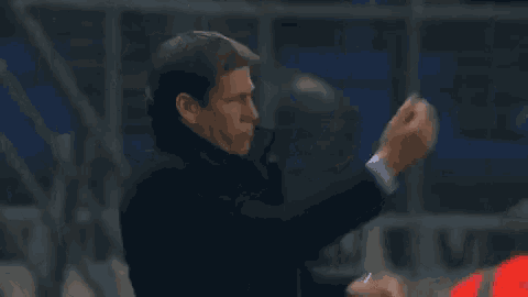 a man in a black coat and white shirt is clapping his hands in the air .
