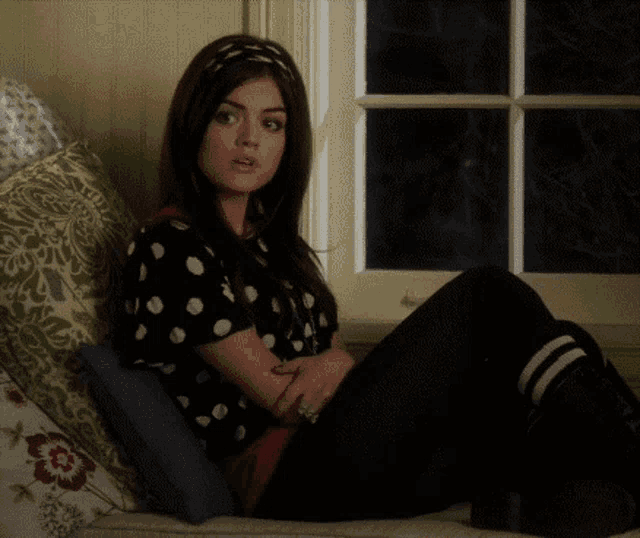 a woman in a polka dot shirt sits on a couch next to a window