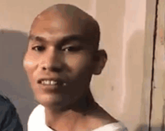 a man with a bald head is smiling and looking at the camera while wearing a white shirt .