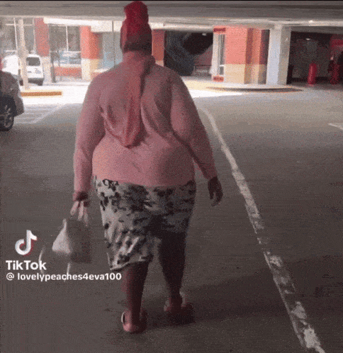 a woman in a pink shirt is walking down a parking lot with a tiktok watermark