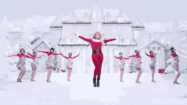 a woman in a santa suit is surrounded by candy cane dancers in front of a white house