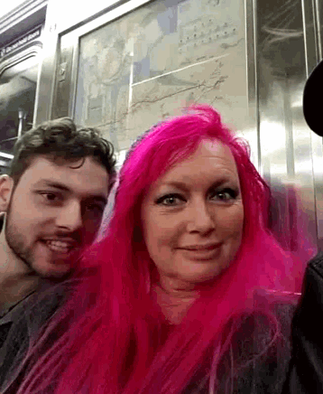 a woman with pink hair is sitting next to a man on a train