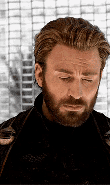 a man with a beard is wearing a black jacket and looking down with his eyes closed .