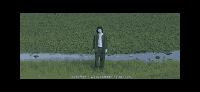a man in a cardigan is standing in a field with a bird flying in the background .