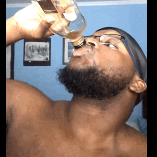 a shirtless man drinking from a glass bottle