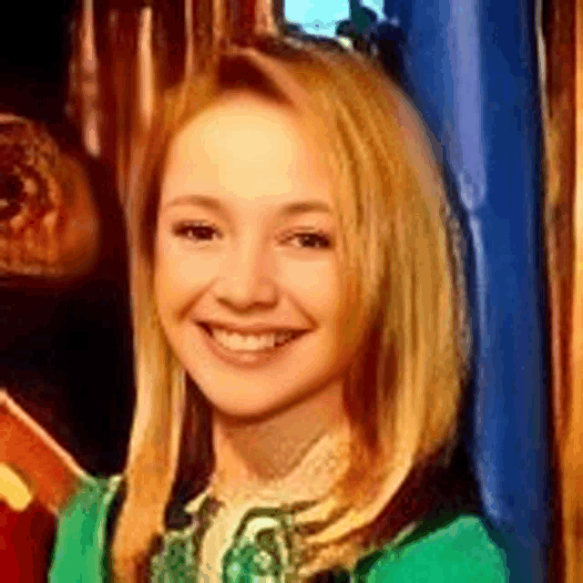 a young woman with blonde hair is smiling and wearing a green sweater .