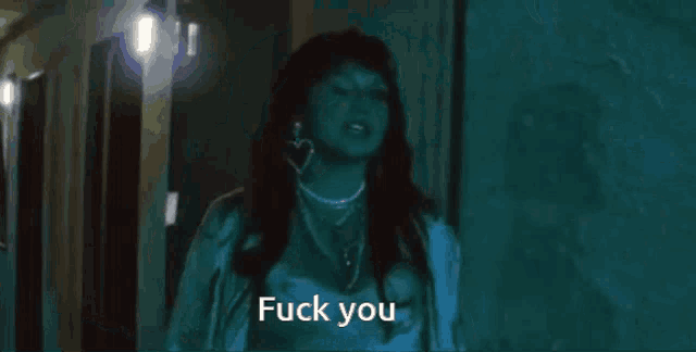 a woman is standing in a dark hallway and says " fuck you " .