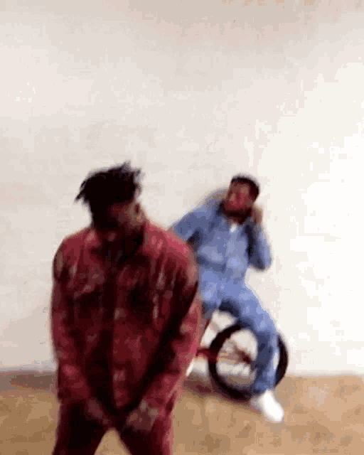 a man in a red jacket is dancing next to a man in a blue suit sitting on a tricycle .