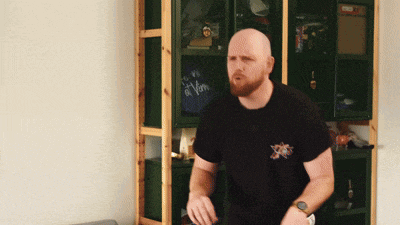 a bald man with a beard is standing in front of a bookshelf with a bag that says vim on it