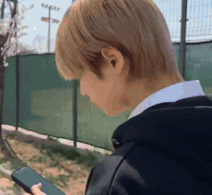 a man is looking at a cell phone in front of a fence
