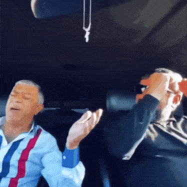two men are sitting in a car with their arms outstretched