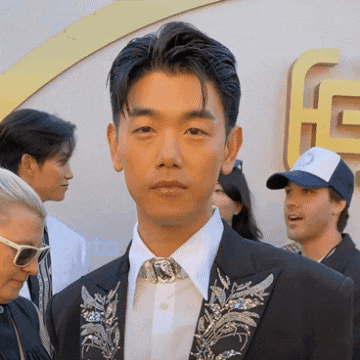 a man in a suit stands in front of a sign that says g