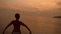 a woman in a bikini stands on a beach watching the sunset over the ocean