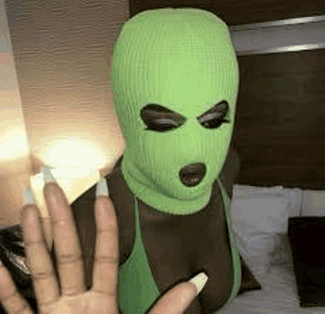 a woman wearing a green ski mask and a green tank top is standing on a bed .