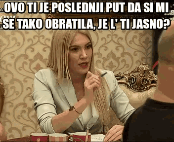 a woman is sitting at a table talking to a man with a caption that says ovo tije poslednji
