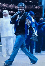 a man wearing a blue jacket with the letter t on it is singing into a microphone