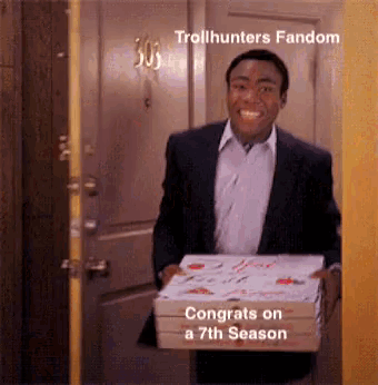 a man in a suit is holding a box of pizza and smiling in front of a door .