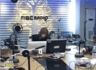 a woman is sitting at a desk in front of a mbc radio sign