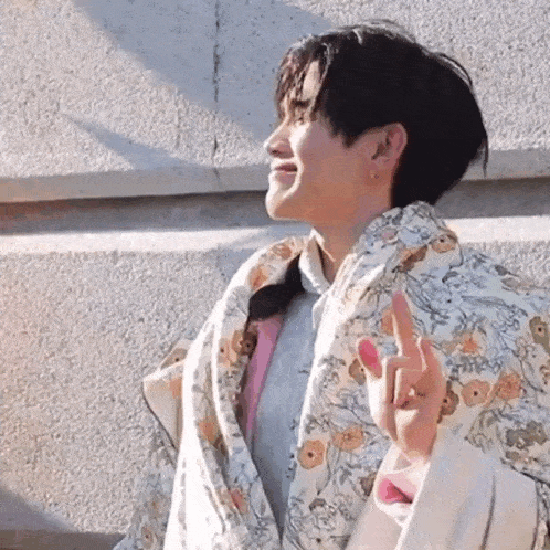 a young man is wrapped in a blanket and making a peace sign with his fingers .