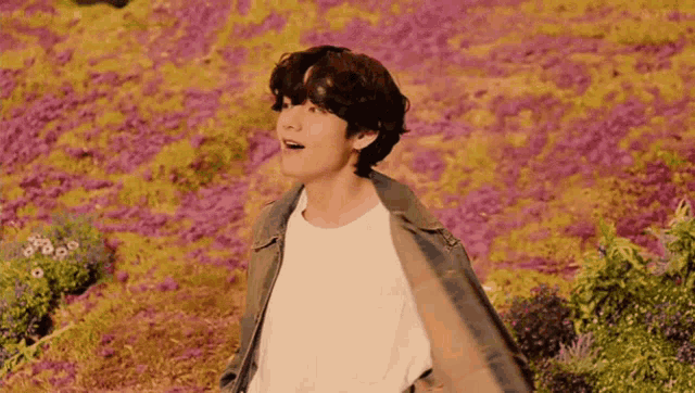 a young man standing in a field of purple flowers .