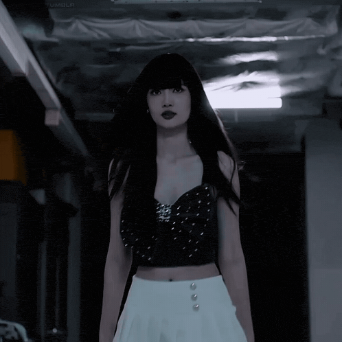 a woman in a black crop top and white skirt stands in a dark room
