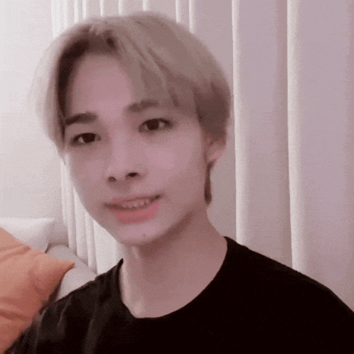 a young man with blonde hair is wearing a black shirt and making a funny face .