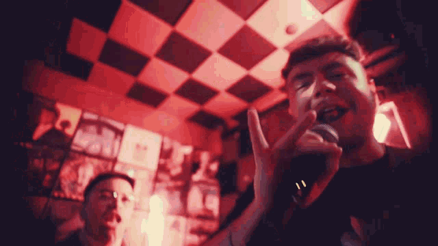 a man singing into a microphone in front of a checkered wall