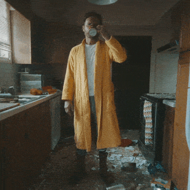 a man in a yellow robe is holding a cup of coffee in a kitchen
