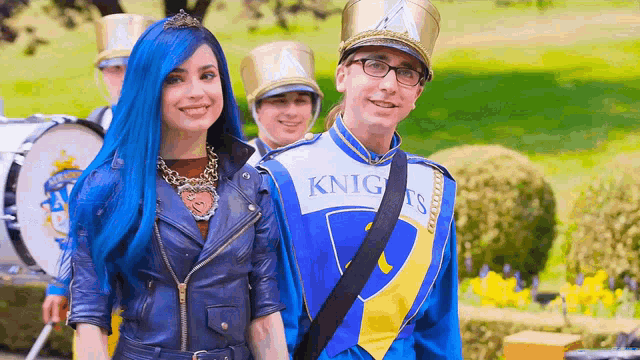 a woman with blue hair and a man in a marching band are standing next to each other .