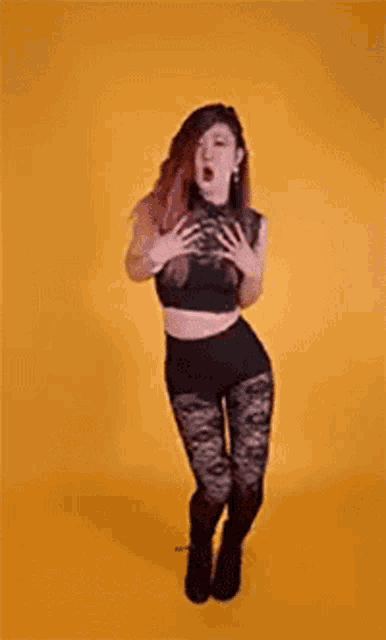 a woman in a black crop top and black pants is standing on a yellow background .