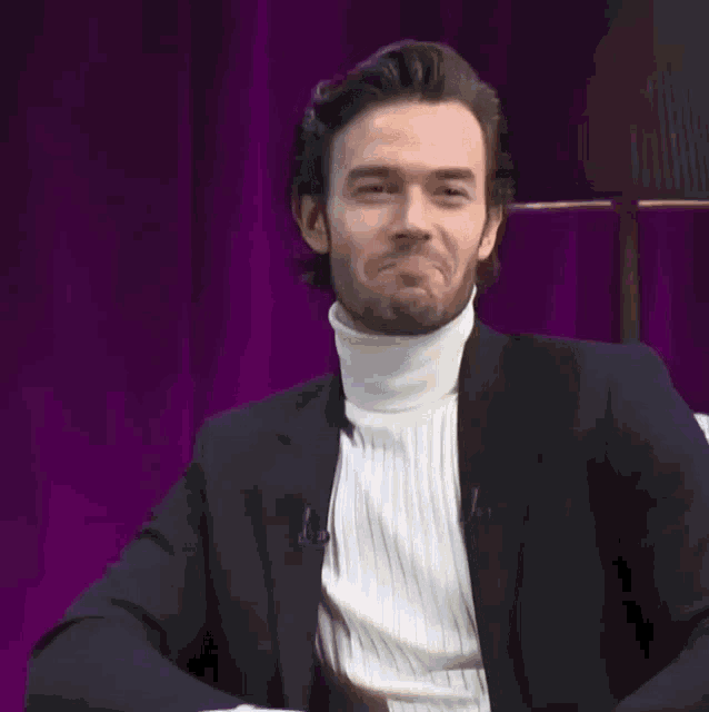a man in a suit and white turtleneck smiles