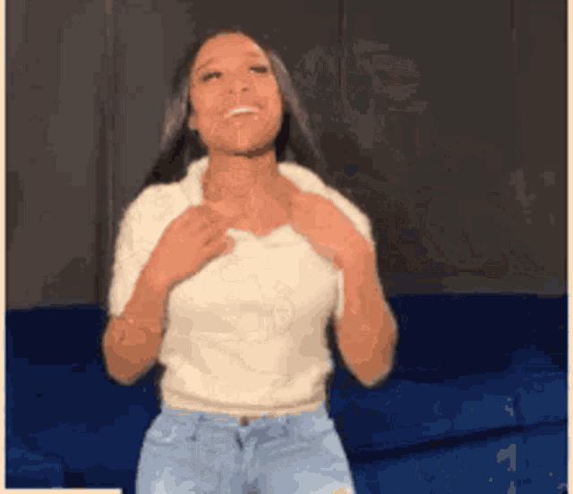 a woman in a white shirt and blue jeans is dancing in front of a blue couch .