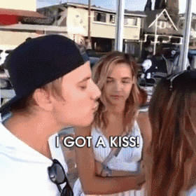 a man in a baseball cap is kissing a woman in front of a group of people and says i got a kiss .