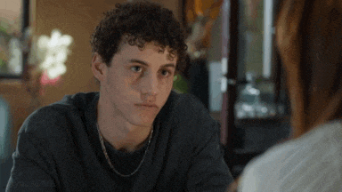 a young man with curly hair is sitting at a table with a woman and looking at the camera .