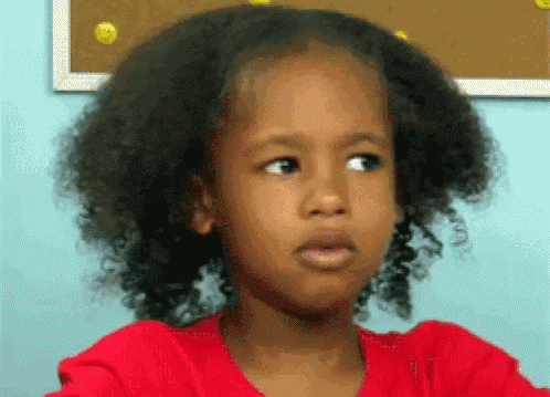 a little girl with curly hair is making a funny face while wearing a red shirt .
