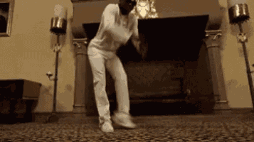 a man in white pants is dancing in front of a fireplace .