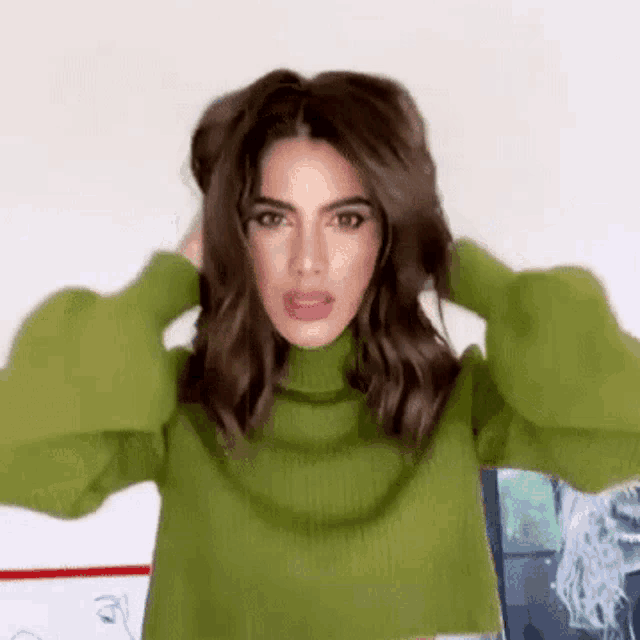 a woman in a green sweater is holding her hair in a bun .