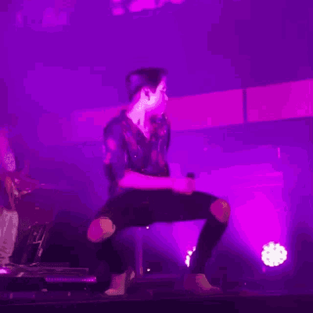 a man is kneeling down on a stage holding a microphone .