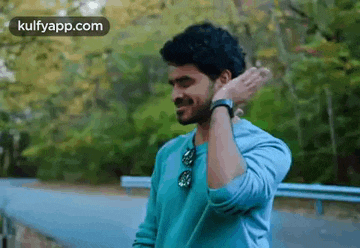 a man in a blue shirt is standing on the side of a road with his hand on his neck .